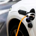 The back left hand side of a white electric car with a white charger plugged in and a yellow cord